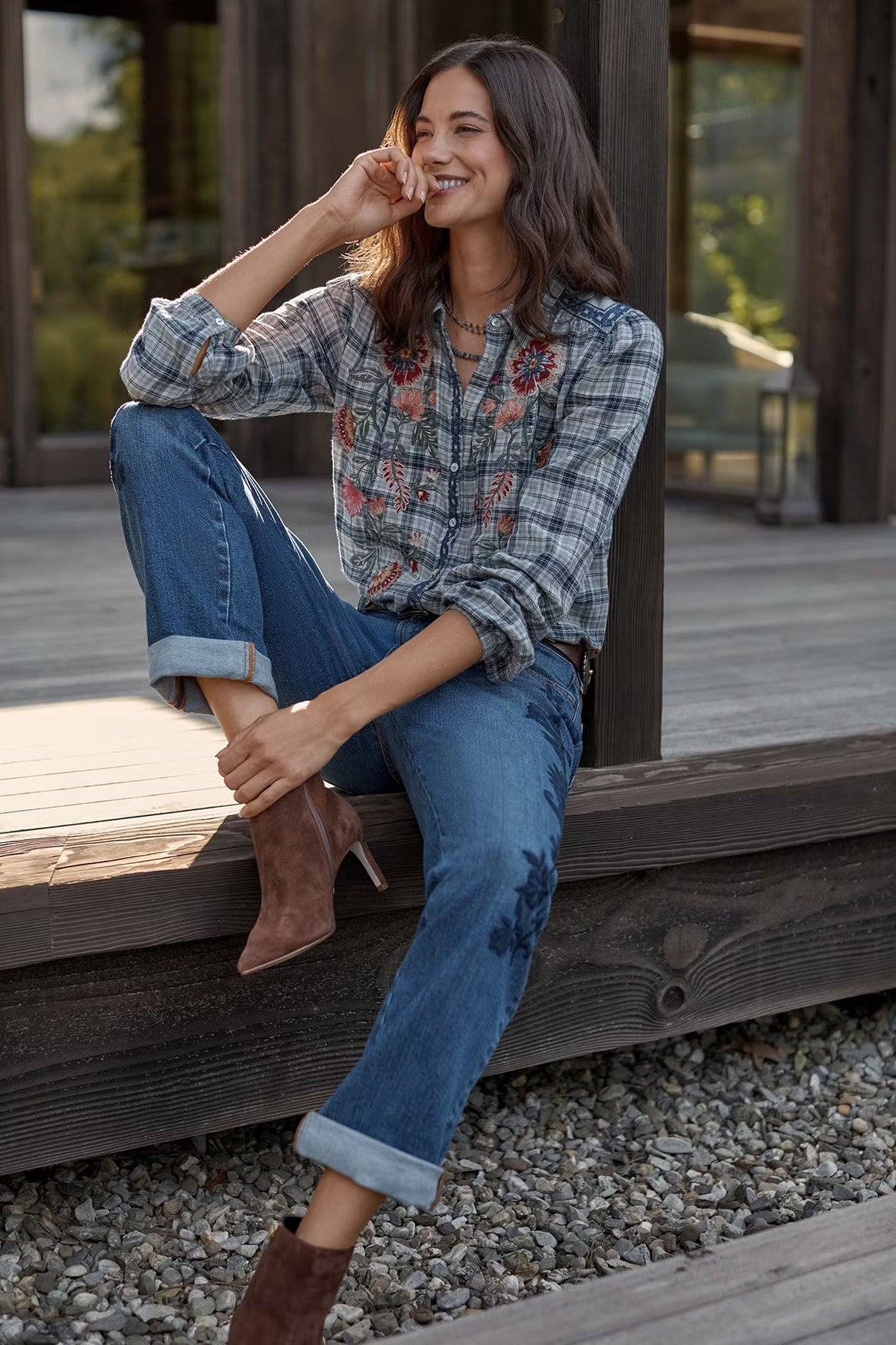 A women on a porch, wearing a Johnny Was Beom Shirt smiling while kicked back and leaning against a post.