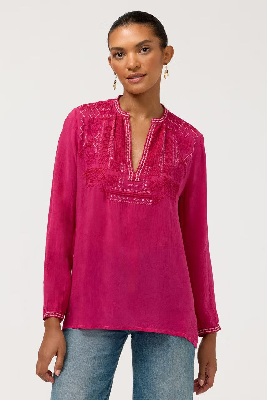 A woman modeling The Johnny Was Wes Blouse in stunning Cherries Jubilee featuring intricate embroidery around the split neckline and yolk. It's paired with blue jeans against a light gray studio background.