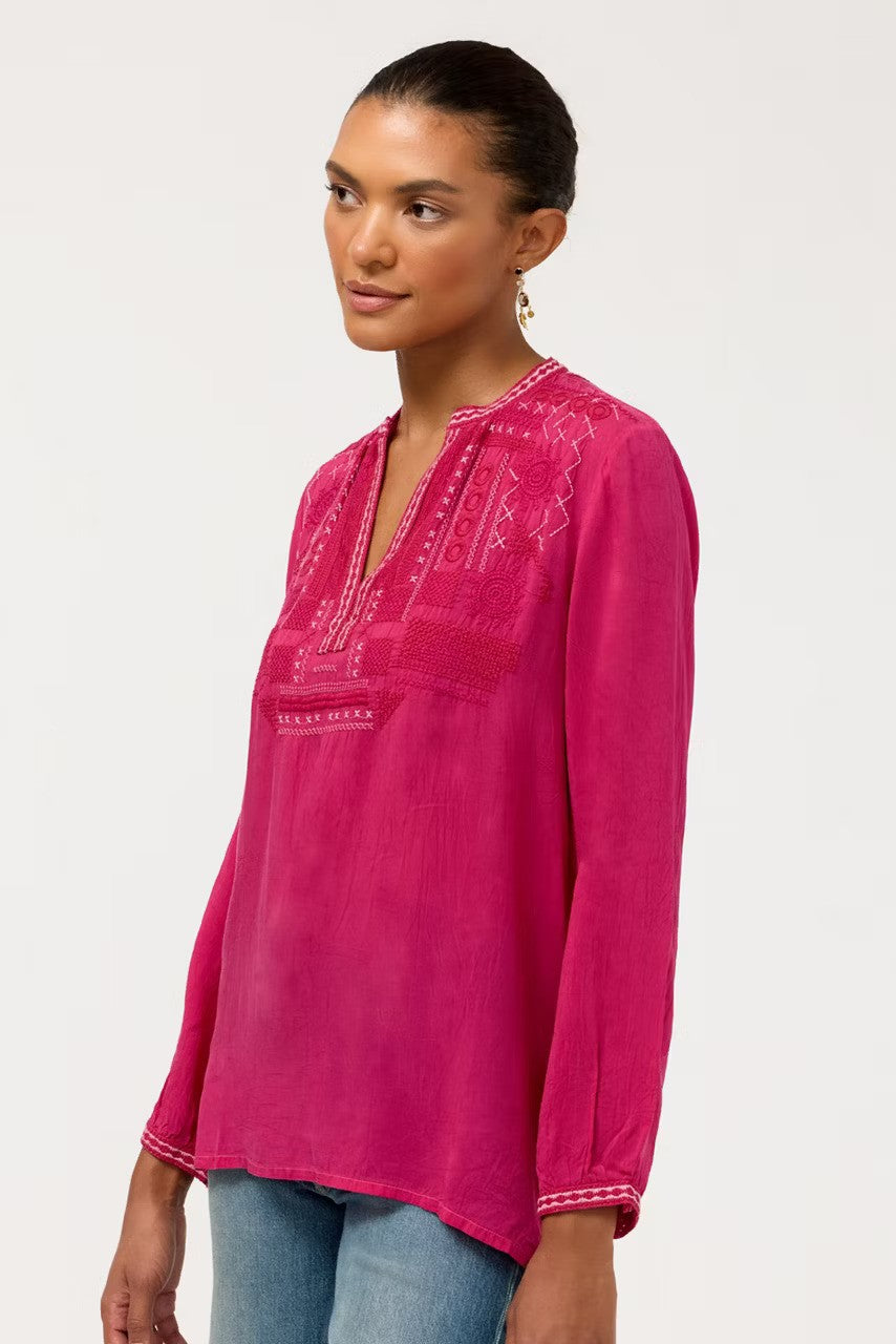 Wearing The Johnny Was Wes Blouse in stunning Cherries Jubilee, and blue jeans, a model is photographed from the side, against a plain light gray background.