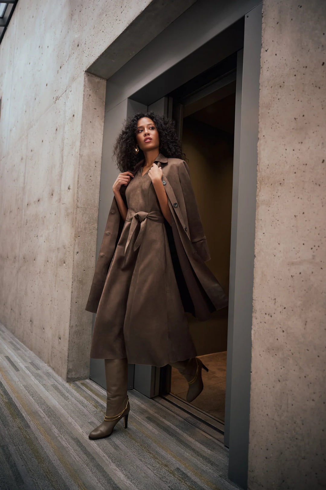 A women walking out of a door wearin Joseph Ribkoff Faux Suede Car Coat draped over her shoulder looking down the street.
