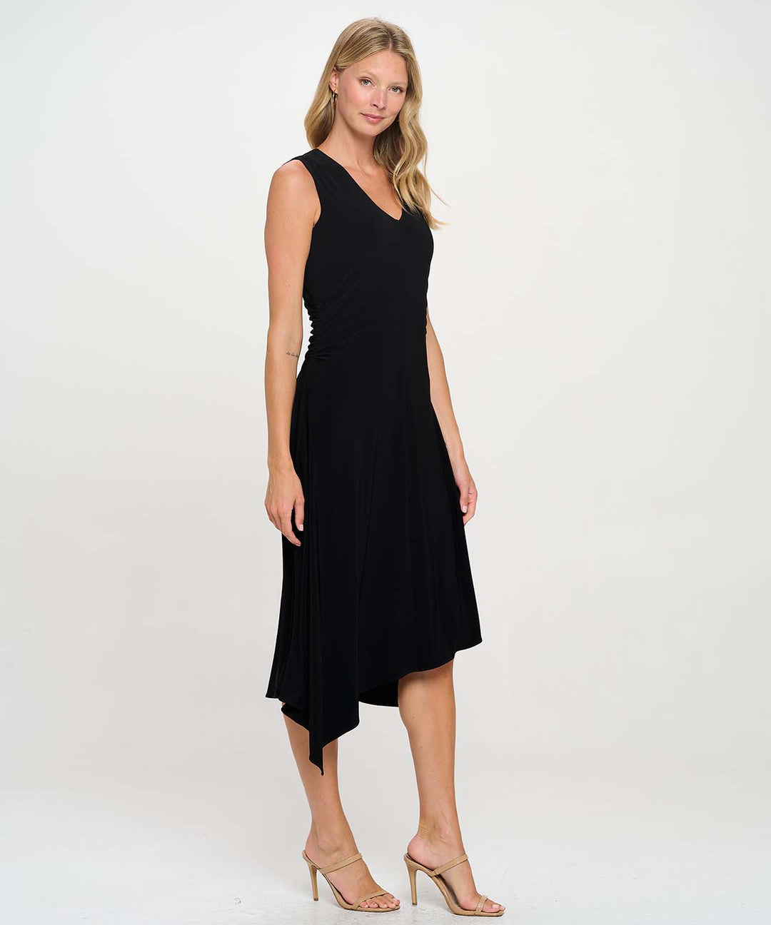 Side view of a woman posing wearing a black Last Tango Asymmetrical Sleeveless V Neck Dress with Side Ruching in front of white background.