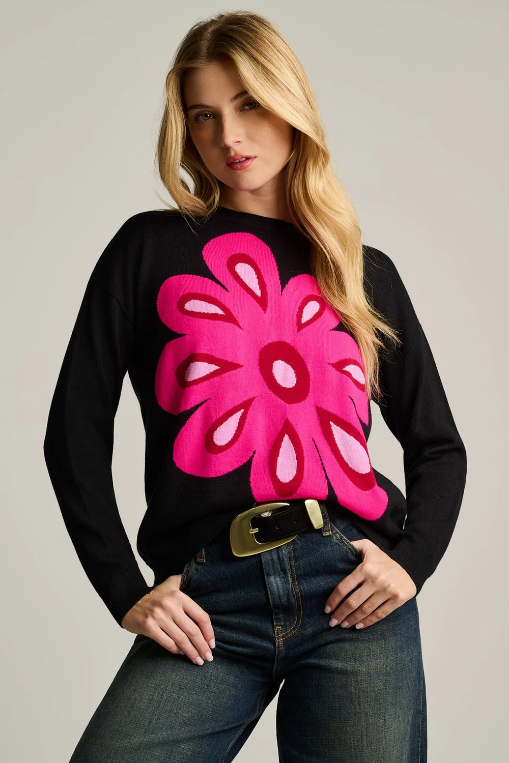 A studio close up of a Women in black Lisa Todd Flower Power Cotton Sweater with her thumbs tucked into the pockets of her blue jeans.