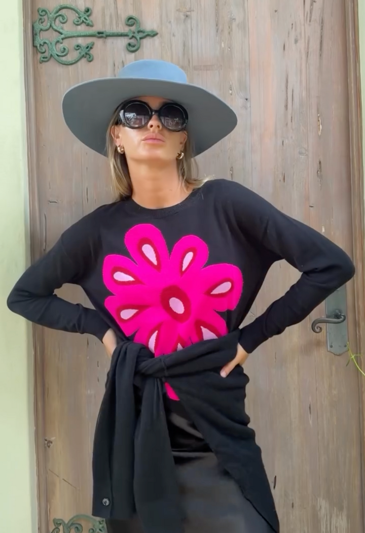 A confident women wearing a black Lisa Todd Flower Power Cotton Sweater, with her hands on hips wearing sunglasses and light blue bolero hat looking directly at the camera.